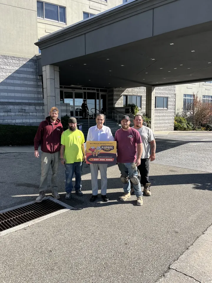Five Plumbing Pals crew members holding the company sign outside a commercial building