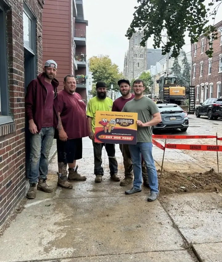 Five Plumbing Pals crew members holding the company sign on a Philadelphia rowhome street with a van behind them