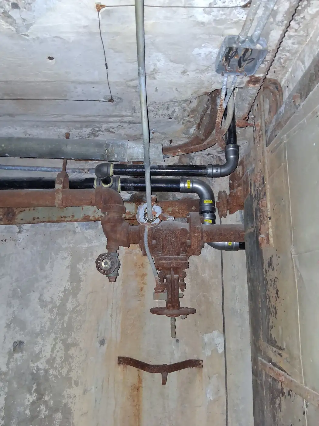 Black iron gas piping with a shutoff valve along a basement wall