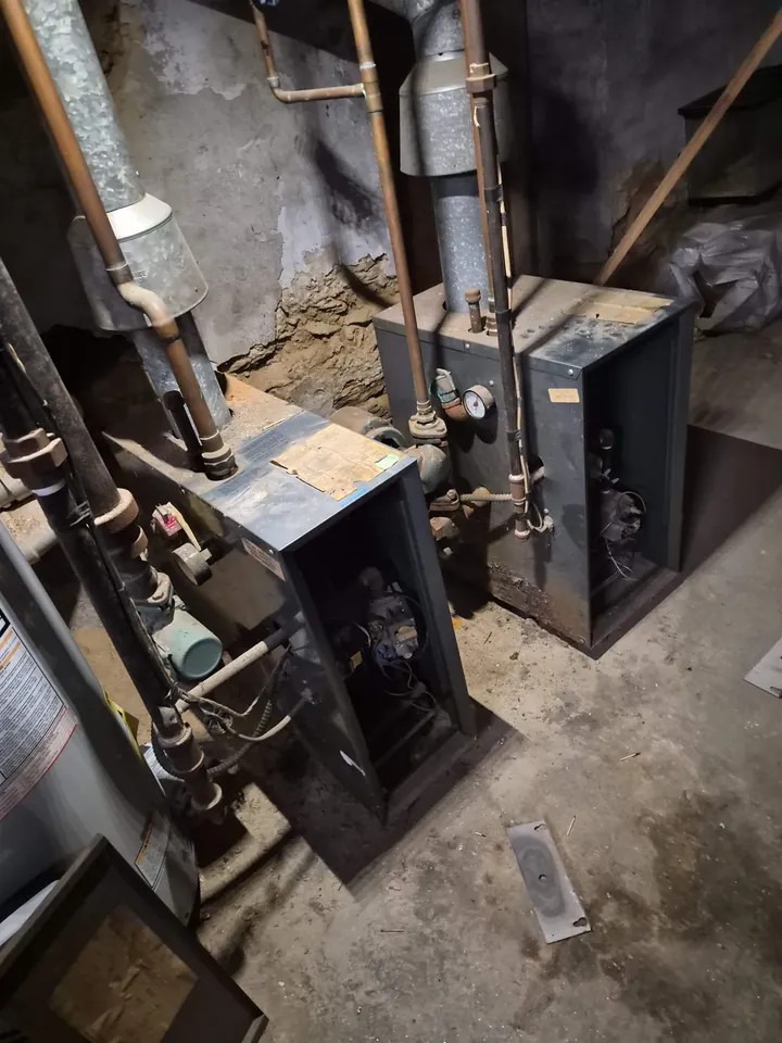 Two aged cast-iron gas boilers in a Philadelphia rowhome basement before replacement
