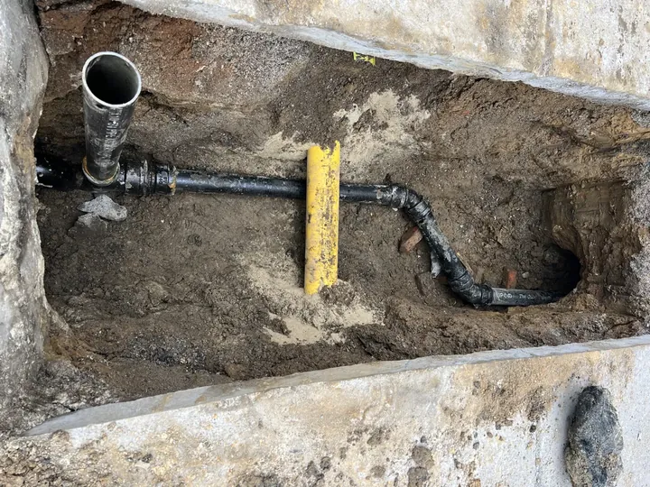 Excavated sewer lateral with new black pipe and fittings beneath a sidewalk