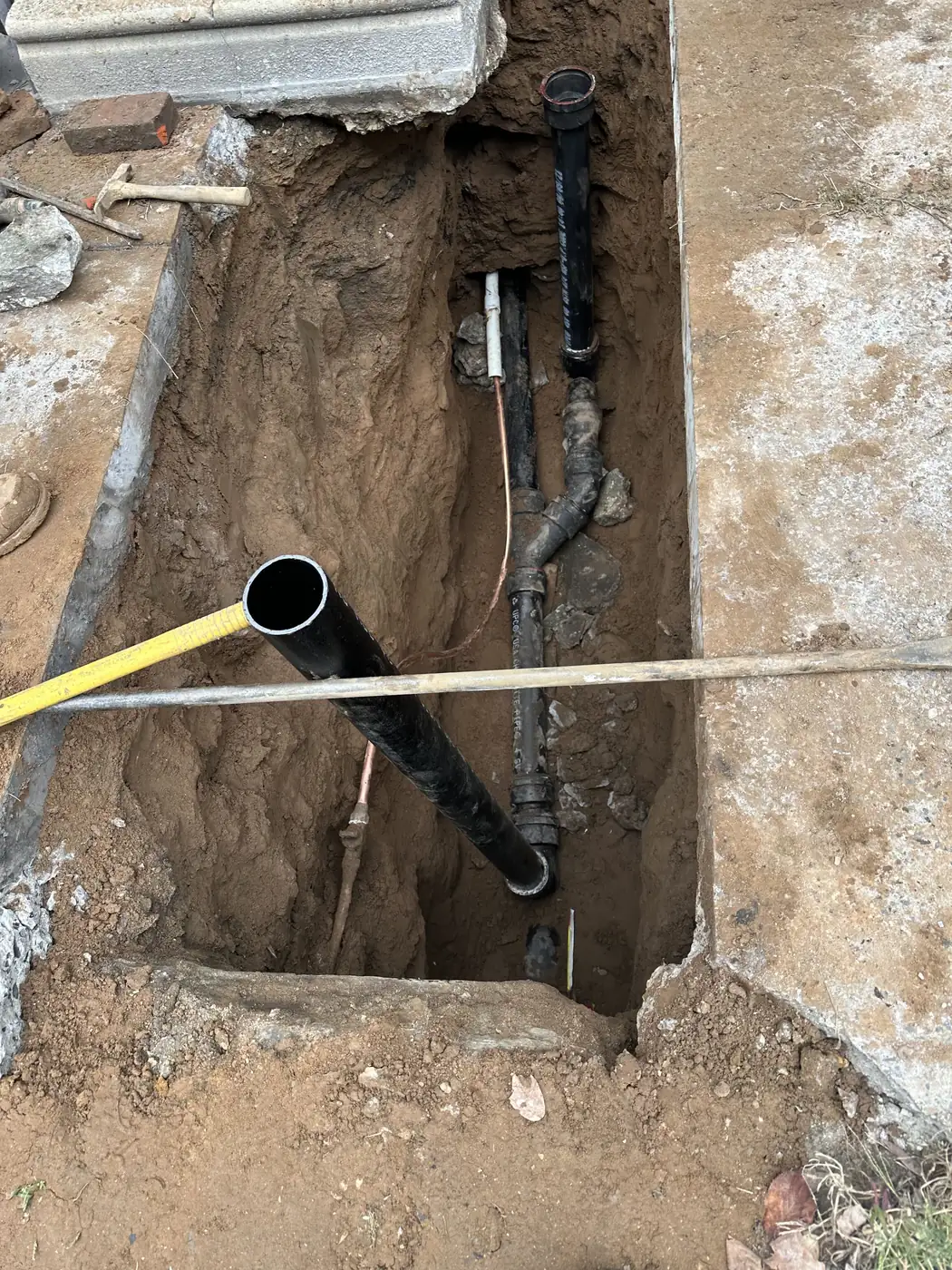 A new black sewer line laid in an open trench beside the sidewalk