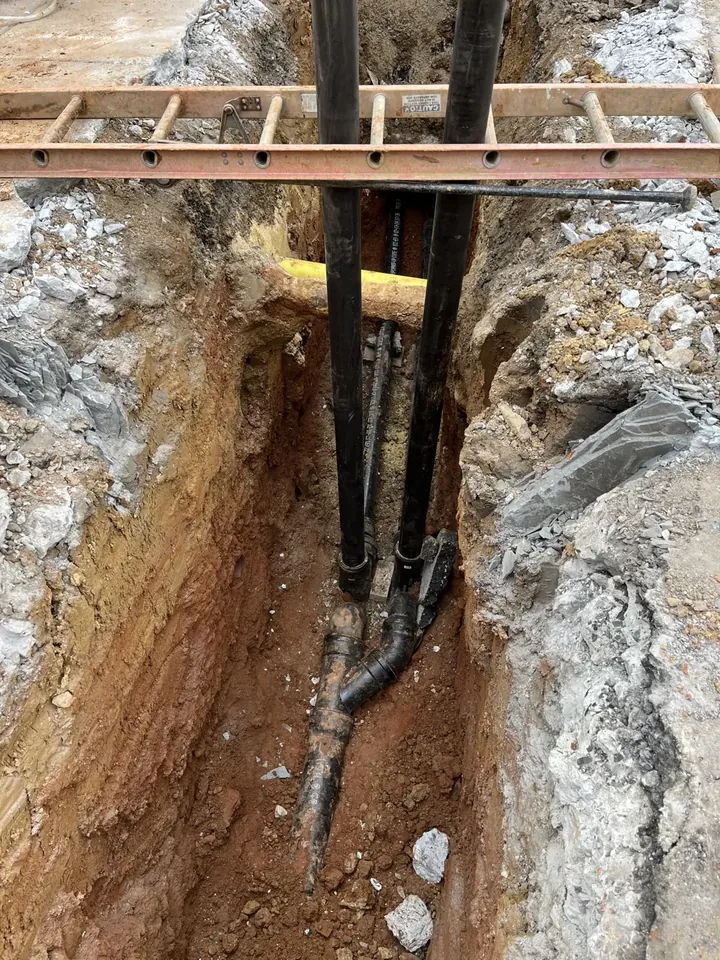Two underground lines exposed in an open excavation with a ladder