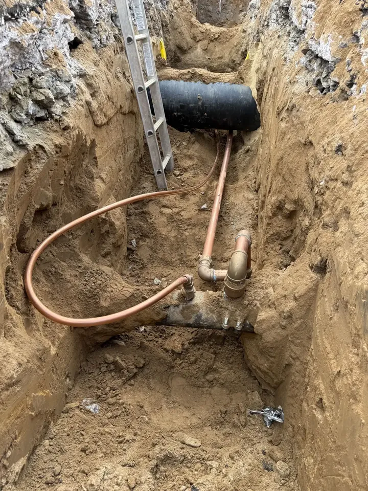 New copper water service line running through an open trench with a ladder set for the crew