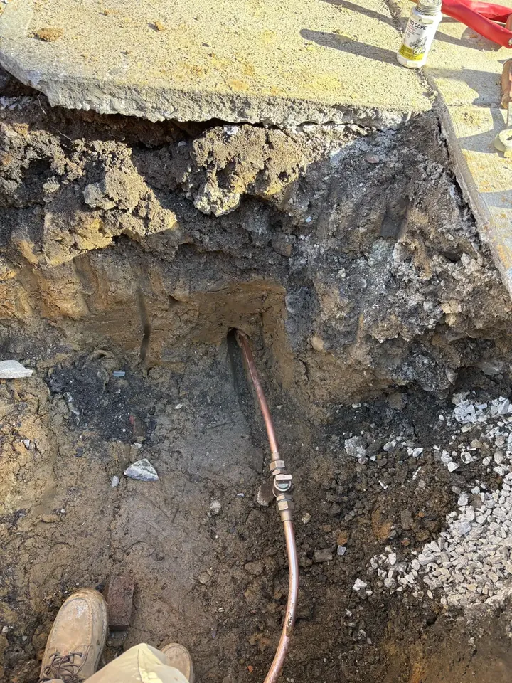Sidewalk-cut excavation exposing a new copper water line and curb stop