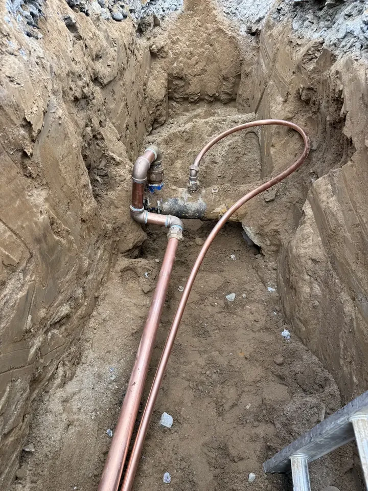 Copper water service line curving through a deep trench toward a house foundation